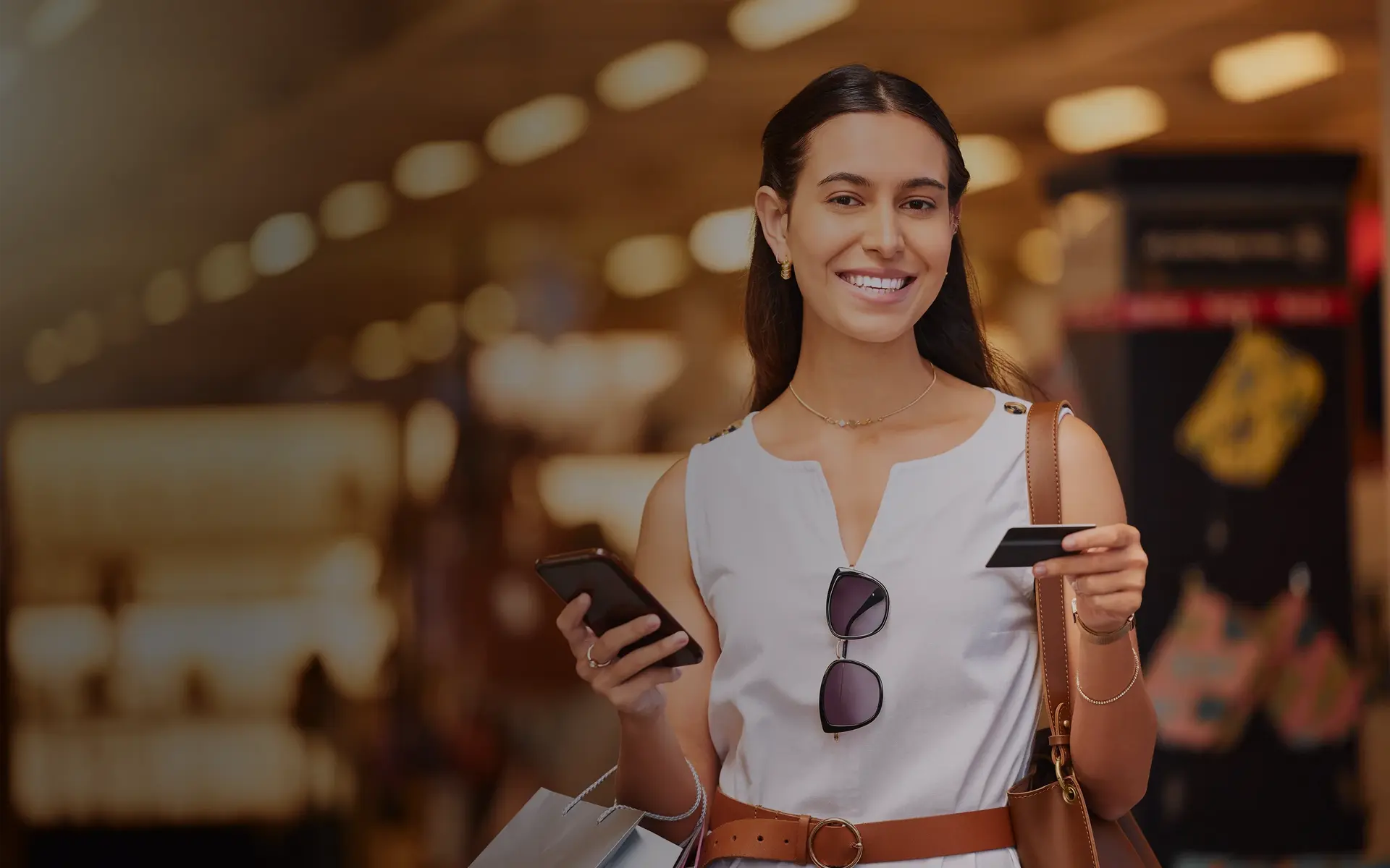 A woman with a shopping bag and a credit card at the mall for fashion.